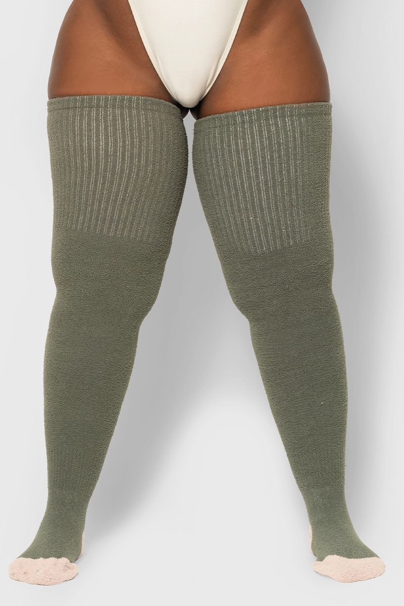 A pair of green, thigh-high socks with a ribbed texture, worn on a model.